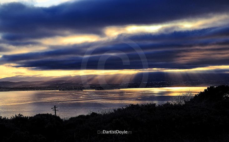 Coucher de soleil sur un lac, avec des nuages sombres et des reflets dorés.