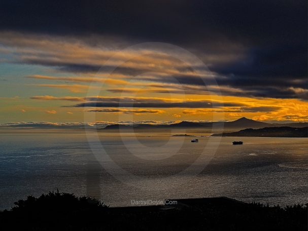 Coucher de soleil sur l'océan avec des nuages et des silhouettes montagneuses au loin.