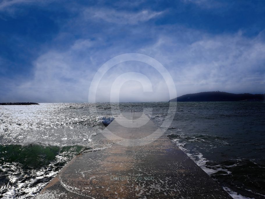 Une jetée s'étend sur l'eau, sous un ciel nuageux et lumineux.