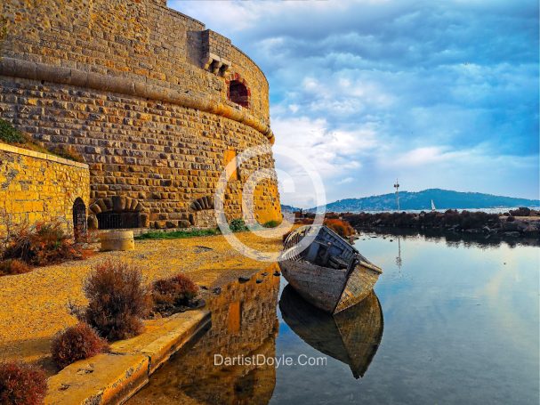 Fortification en pierre au bord de l'eau, avec un bateau échoué et un ciel nuageux.