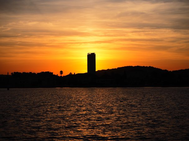 Silhouette d'un gratte-ciel contre un coucher de soleil sur un lac.