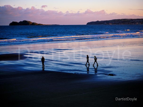 Trois personnes marchent sur la plage au coucher du soleil, avec des vagues doucement déferlantes.