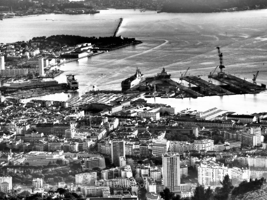 Vue en noir et blanc d'un port avec des bâtiments et des bateaux sur l'eau.