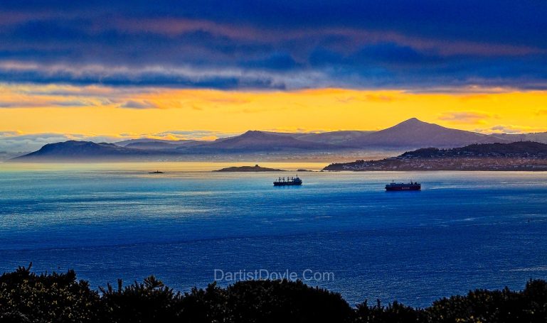 Paysage côtier avec des bateaux au coucher du soleil et des montagnes en arrière-plan.