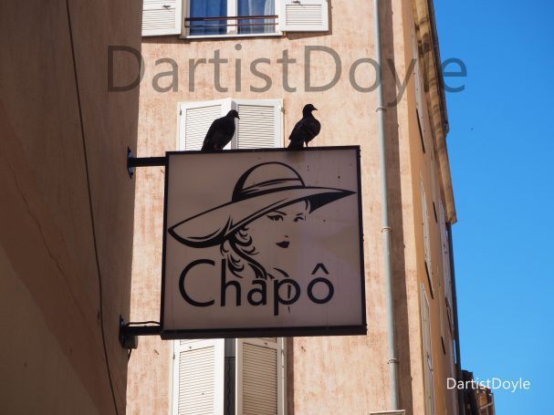 Panneau de boutique avec un dessin d'une femme au chapeau et deux oiseaux perchés.