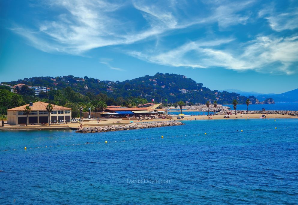 Vue d'un littoral méditerranéen avec des plages, des palmiers et une villa en arrière-plan.
