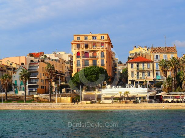 Bord de mer avec des bâtiments colorés et des palmiers au soleil.